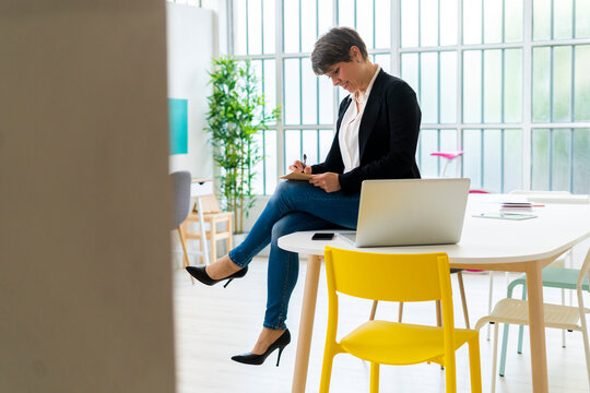 Female professional writing while siting on desk in office