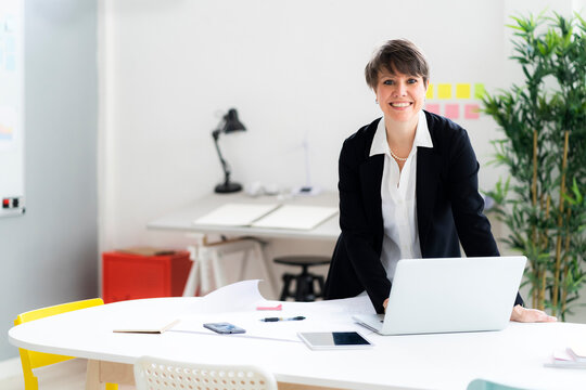 Smiling Businesswoman With Laptop Standing At Desk In Office