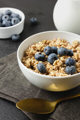 Granola with blueberry in white bowl on dark napkin.