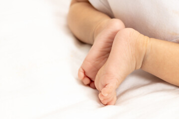 close up asian woman small baby infant feet while sleeping on soft bed covered with white cloth.