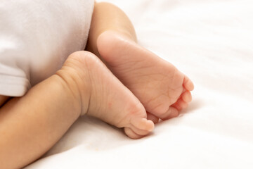 close up asian woman small baby infant feet while sleeping on soft bed covered with white cloth.