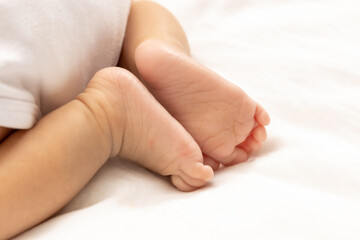 close up asian woman small baby infant feet while sleeping on soft bed covered with white cloth.