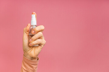 Close-up photo of senior mature aged woman's hand holding sanitizer spray washing cleaning hands health quarantine isolated over pink background.
