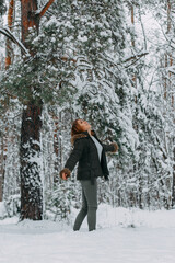A happy girl with a short haircut walks in the forest after a snowfall and admires the incredible nature. Winter fairy tale in the forest. Christmas holidays, outdoor activities