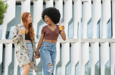 Cheerful female friends holding hands while walking in city