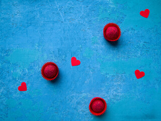 Red candy and red hearts on a bright blue background. Three chocolate truffles decorated with sublimated raspberries. Symbol of love.