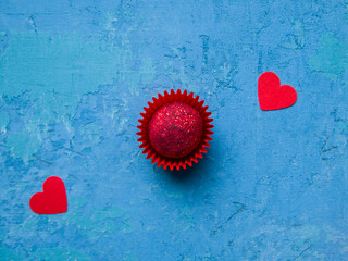 One pink chocolate truffle topped with sublimated raspberries on a bright blue concrete background. Next to this are two red hearts. Romantic concept.