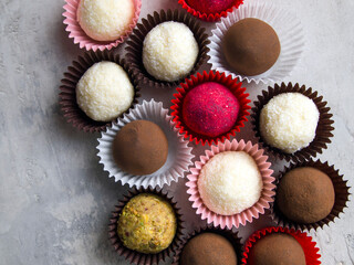 Top view on truffle sweets in wrappers. Different types of candy: dark chocolate truffle in cocoa, white coconut truffle, red candy covered with sublimated raspberries, candy covered in nut crumbs.