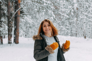 Portrait of a happy girl with a short haircut in mustard mittens in the forest after a snowfall . Christmas holidays, outdoor activities