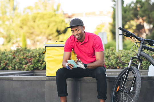Smiling delivery man using mobile phone while sitting on bench