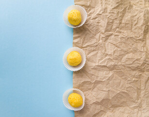 Top view of three chocolate truffles in white candy wrappers on a blue and beige background. Golden yellow citrus flavored sweets.