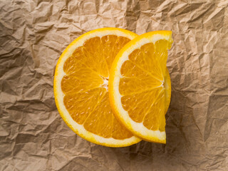 Top view of half an orange on which lies a slice of fruit. Natural sweet dessert lies on dark brown crumpled kraft paper.