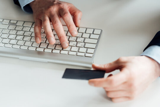 Businessman holding card while typing on computer keyboard in office