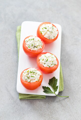 Fresh tomatoes stuffed with cottage cheese and parsley on a serving tray on a light gray background. Top view