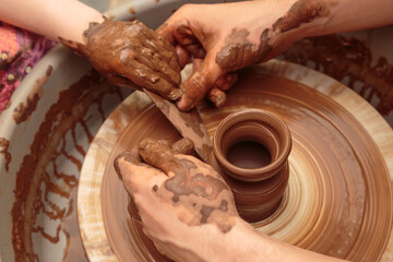 The child moulds from clay a pot on a potter's wheel. Adults help the child to work with clay.