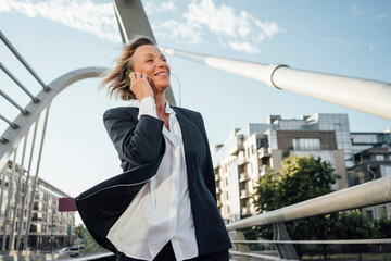 Mature businesswoman looking away while talking on smart phone in city