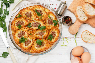 Delicious homemade baguette casserole with minced meat, egg, parsley and spices. Savory bread pudding. Breakfast. Brunch. White wooden table. Selective focus, top view