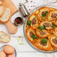 Delicious homemade baguette casserole with minced meat, egg, parsley and spices. Savory bread pudding. Breakfast. Brunch. White wooden table. Selective focus, top view