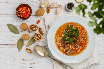Kharcho soup. Thick beef soup with rice, tomatoes, peppers, walnuts, cilantro, garlic and spices on a white wooden background. traditional dish of Georgian cuisine. Top view