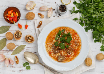 Kharcho soup. Thick beef soup with rice, tomatoes, peppers, walnuts, cilantro, garlic and spices on a white wooden background. traditional dish of Georgian cuisine. Top view