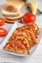 Homemade mini pizzas made of toast bread with ham or sausage, tomatoes, parmesan cheese and mozzarella and spices. Breakfast. White plate, wooden background. Brunch. Selective focus