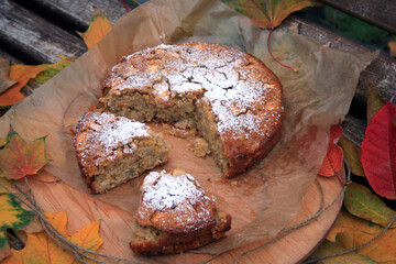 Top view of a delicious homemade apple pie cut into pieces. Cupcake decorated with icing sugar. Around this lie dry yellow, orange and red leaves. Autumn atmosphere.