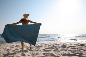 Woman with beach towel and straw hat on sand near sea, back view. Space for text