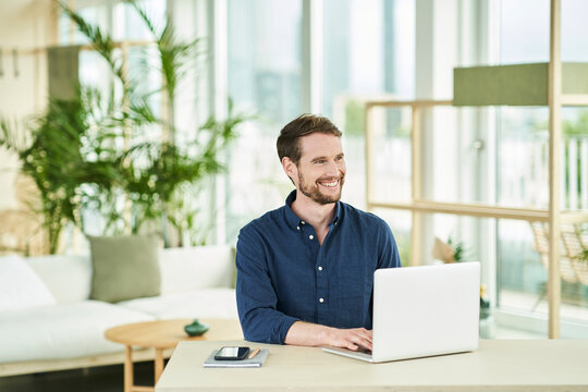 Happy male professional with laptop sitting in home office - Powered by Adobe