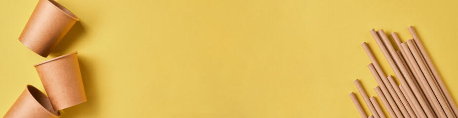 Brown paper drinking straws and eco paper glasses cornstarch, biodegradable material on yellow color background. Zero waste and plastic free concept. Top view. Banner.