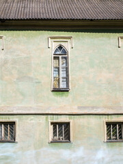 The facade of the old building on which there is one arched window and three square windows. All of them are closed and protected by a metal grill. The wall is light green (parakeet, seafoam, lime).