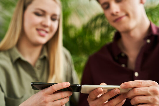 Young businessman with female intern using charge sharing technology through smart phones in office