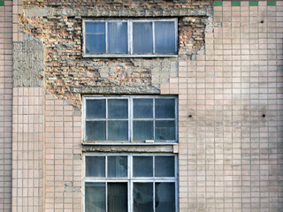 A fragment of the exterior of an old abandoned industrial building. Unpleasant place. Part of the tile fell away, a brick base is visible under it.