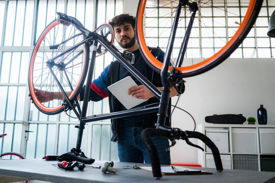 Man with digital tablet holding bicycle wheel at home