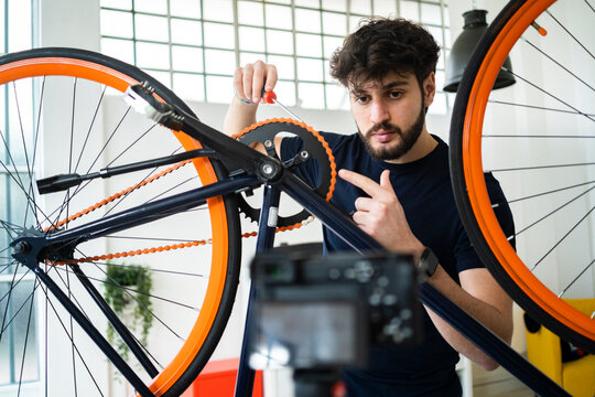 Male vlogger pointing at bicycle chain while filming tutorial at home