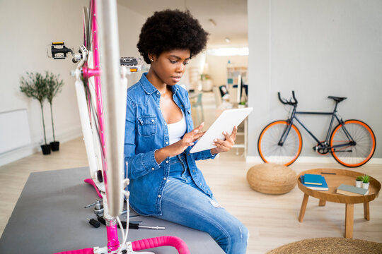 Afro woman watching tutorial on digital tablet while repairing bicycle at home - Powered by Adobe