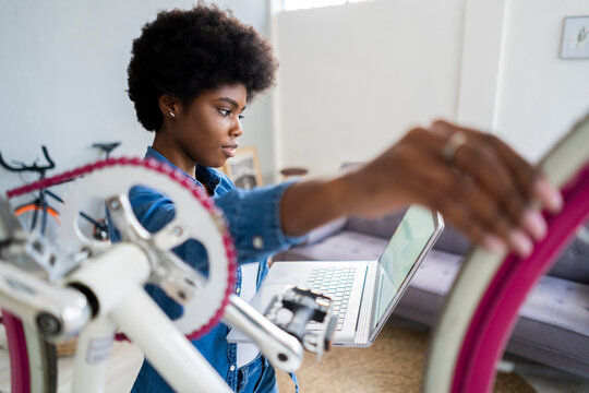 Afro hairstyle woman watching tutorial on laptop while repairing bicycle at home