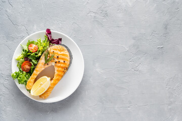 Grilled salmon fish steak with lettuce and tomatoes on a white ceramic plate
