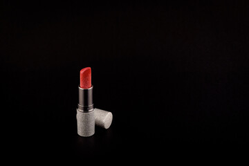 Red lipstick with glitter in a silver bottle cap next to the bottle on a black background side view
