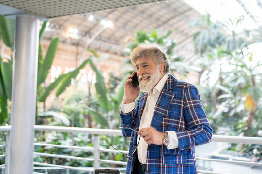 Happy mature man wearing blue plaid blazer talking on mobile phone at station