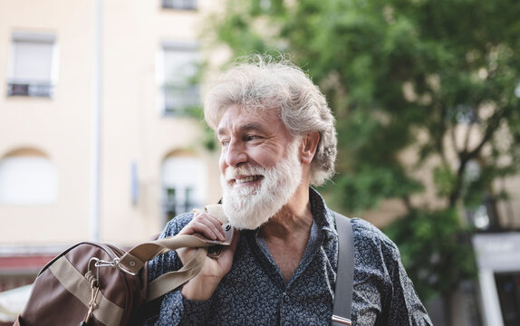 Happy Mature Man With White Hair Looking Back Over Shoulder While Carrying Luggage