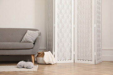 Stylish room with folding screen and sofa near white wall. Interior design