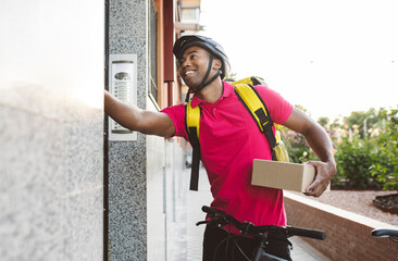 Smiling male delivery person holding package while ringing doorbell