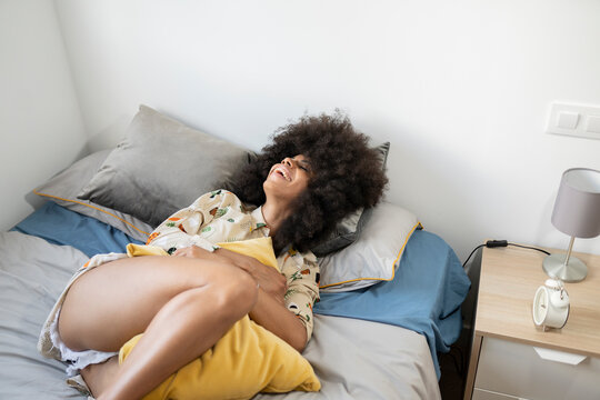 Smiling afro woman lying on bed at home