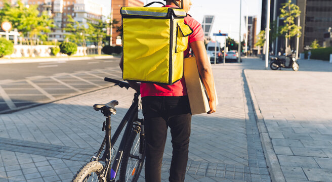 Delivery man carrying package while walking with bicycle on road