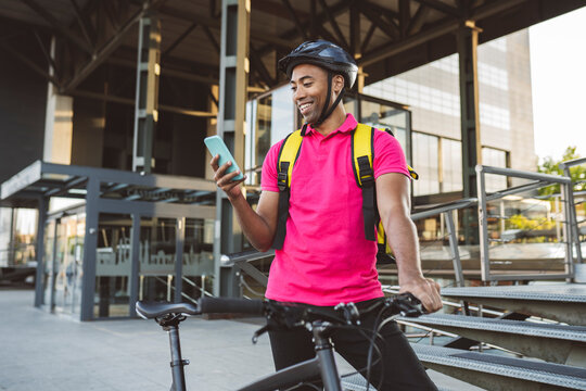 Smiling delivery man text messaging through smart phone while standing with bicycle