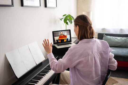 Mid adult woman learning piano with online tutorial on laptop at home