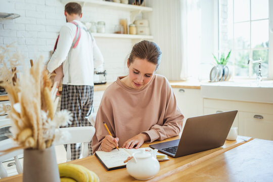 Businesswoman writing on diary with man and daughter in kitchen at home - Powered by Adobe