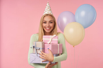 indoor portrait of young blonde female, wears green dress, party hat posing over pink background