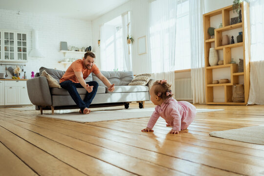 Father calling daughter crawling on floor at home