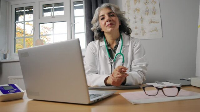 Portrait Of Mature Female Doctor Wearing White Coat At Desk In Office